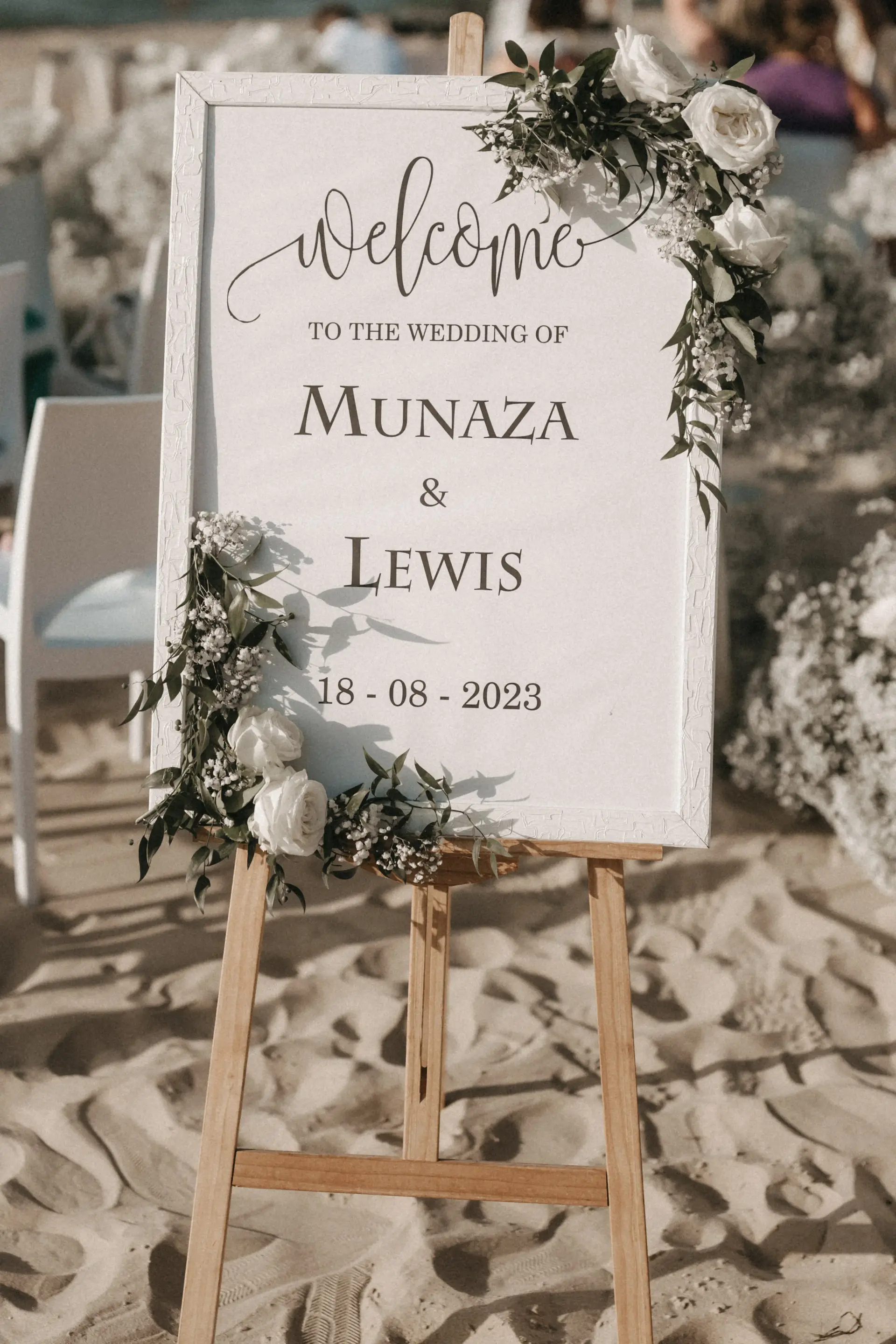 Welcome sign at the beach wedding of Munaza and Lewis on August 18, 2023, decorated with white roses and displayed on a wooden easel in Alcamo Marina, Sicily